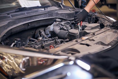 FixBros mechanic inspecting an engine bay with a work light